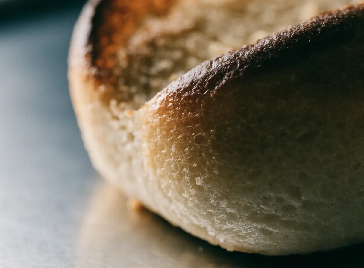 Macro of a toasted potato bun edge with a butter-browned crust on a steel surface